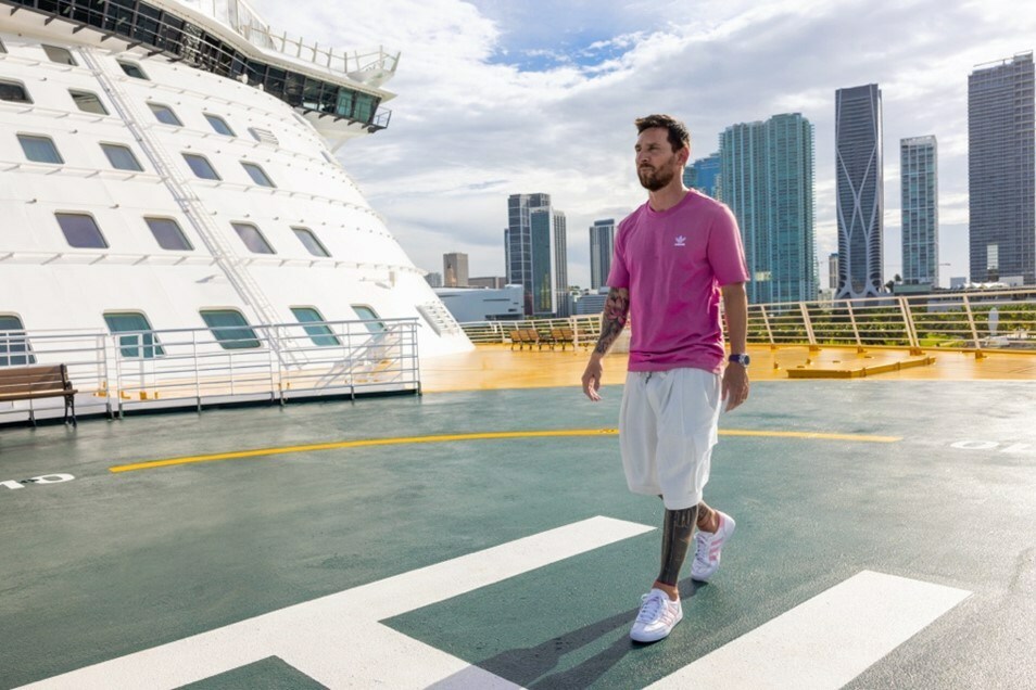 Lionel Messi, in a pink shirt, walks the deck of a Royal Caribbean ship with the Miami skyline in the background.